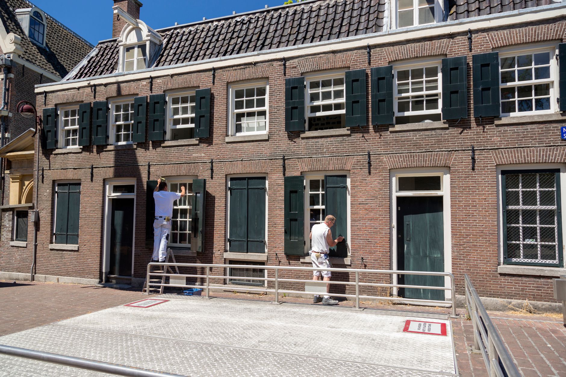 Schilder aan het werk bij de kozijnen van een klassieke bakstenen gevel