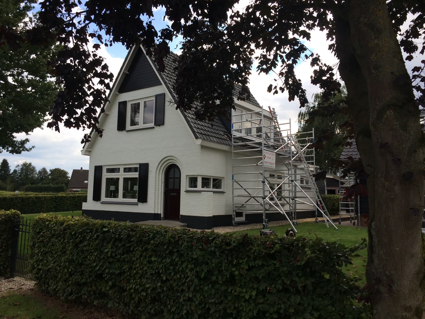 Witte woning met zwarte luiken, met een steiger aan de zijgevel tijdens het schilderwerk