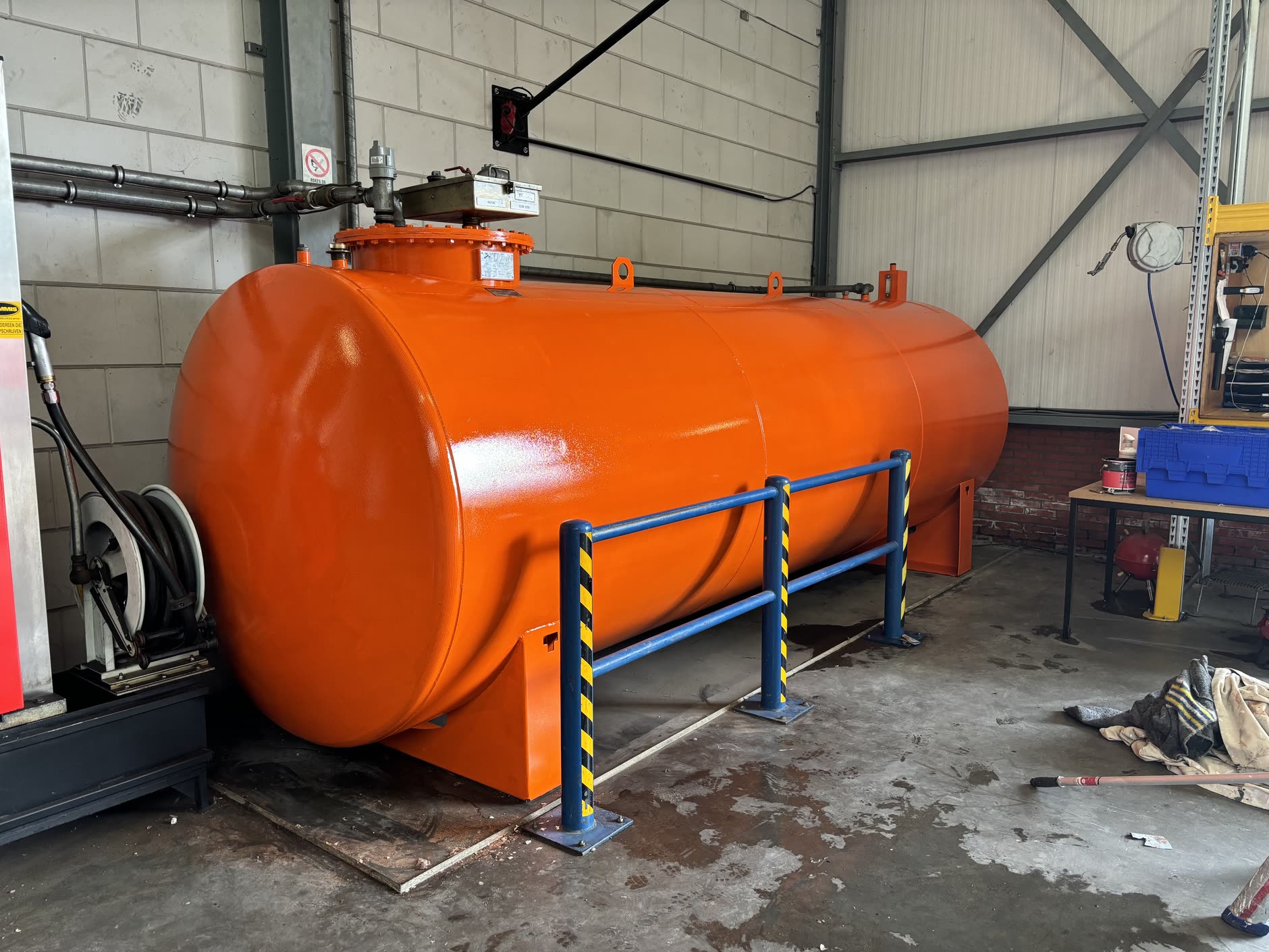 Oranje geschilderde opslagtank in een bedrijfshal, met geel-zwarte aanrijdbeveiliging