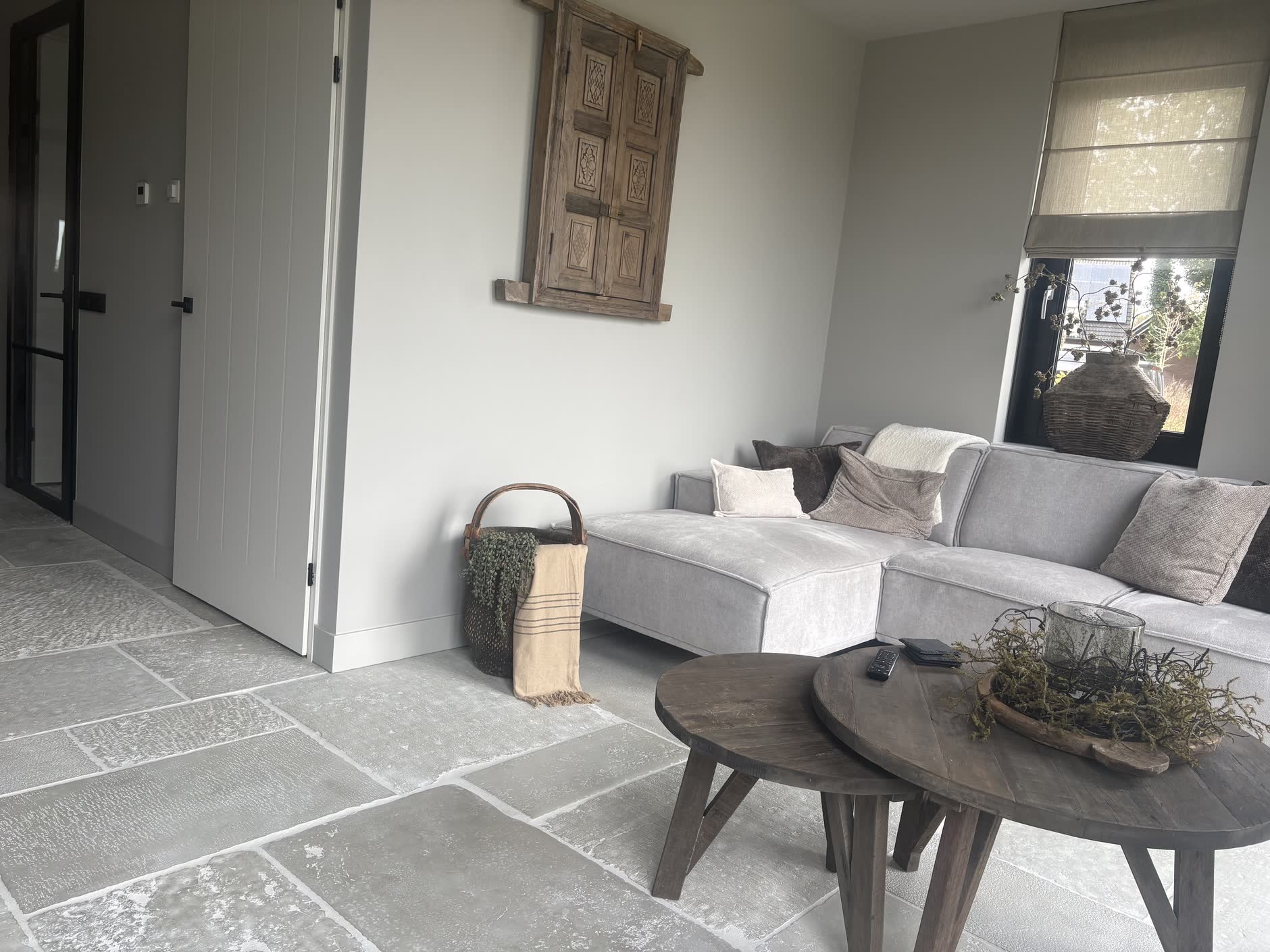 Lichte woonkamer met strak geschilderde wanden, een grijze bank en een natuurstenen vloer
